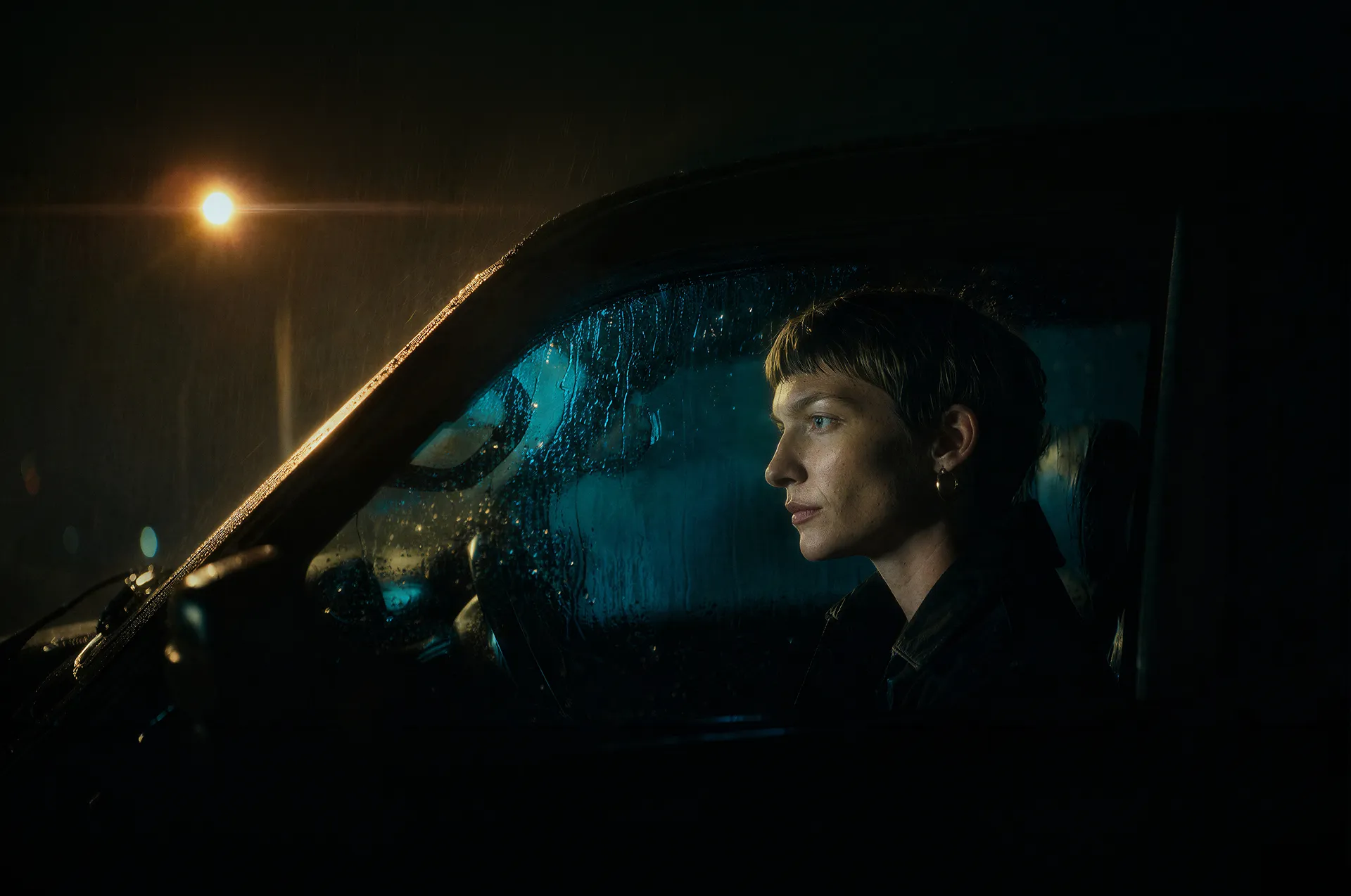 Person gazing through a rain-streaked window at night
