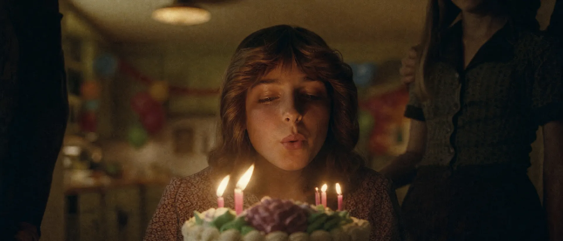 Girl blowing out candles on a birthday cake in warm 1970s light